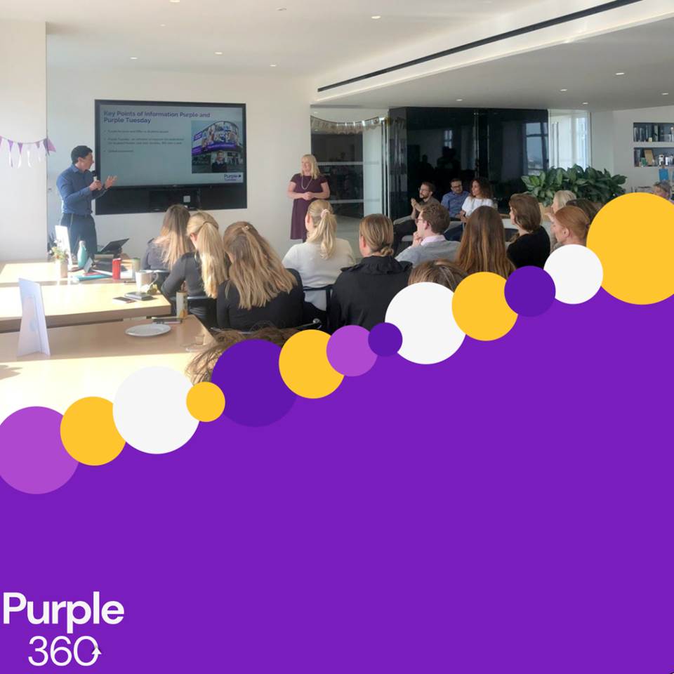 Image of Purple team giving a presentation to a room of people, half purple with yellow and purplecircles.