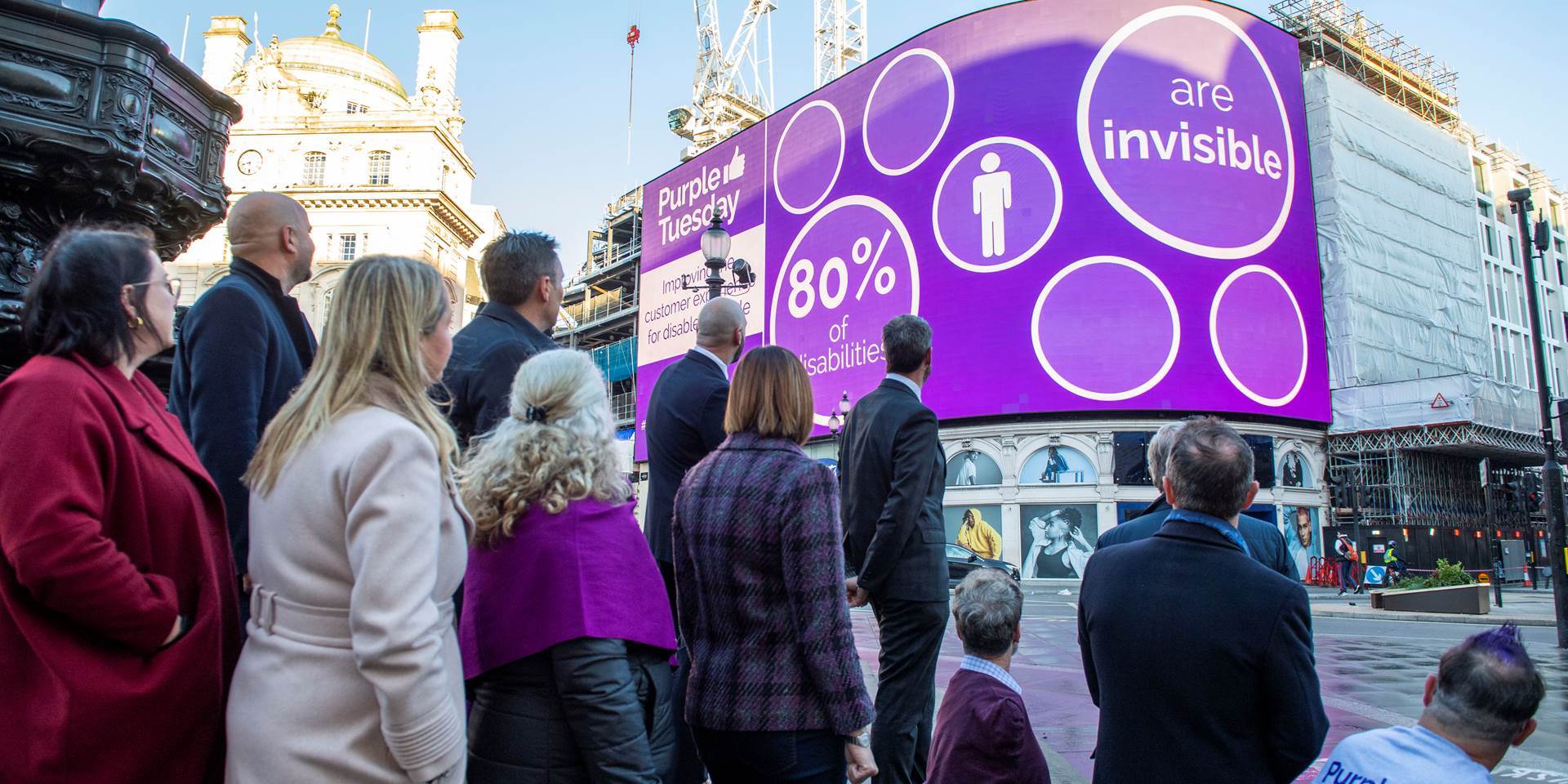 The Purple Tuesday team in Piccadilly Square, observing the illuminated Piccadilly lights adorned with Purple Tuesday branding.