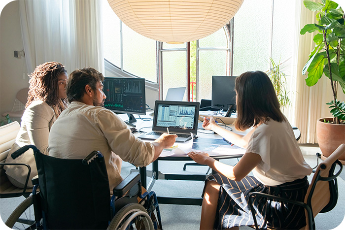 A group of business people sitting focused on laptops, one of which is in a wheelchair